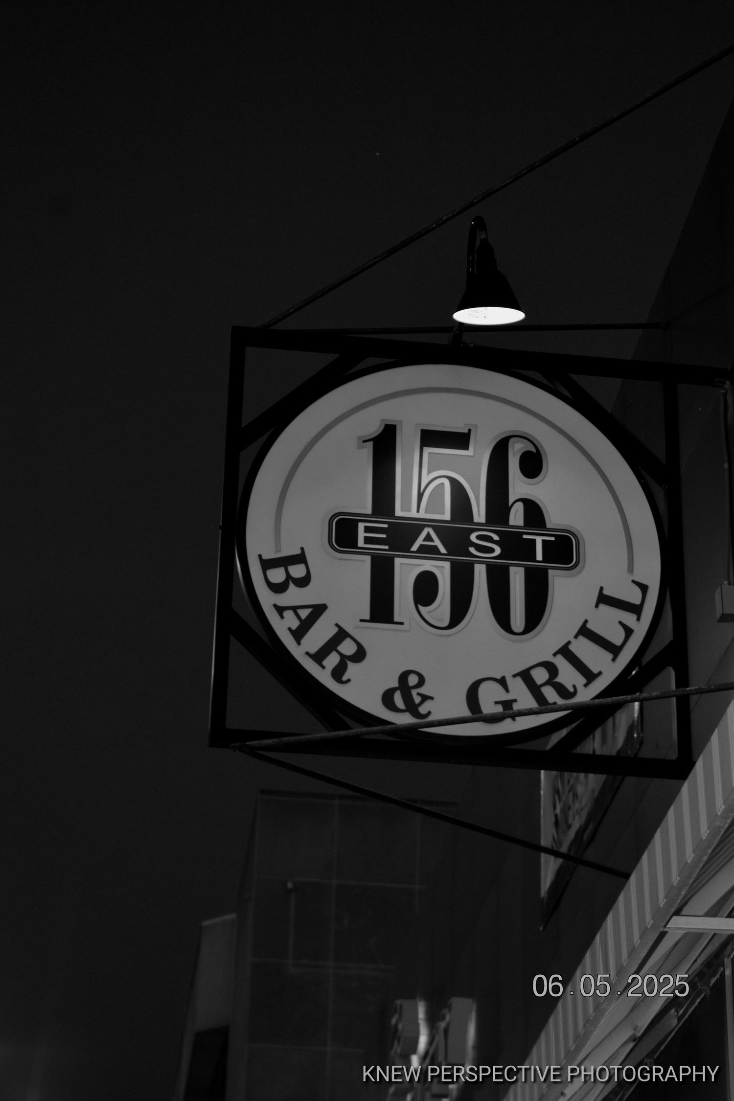 Black and white signage showing '156 East Bar & Grill' text in dark moody lighting.