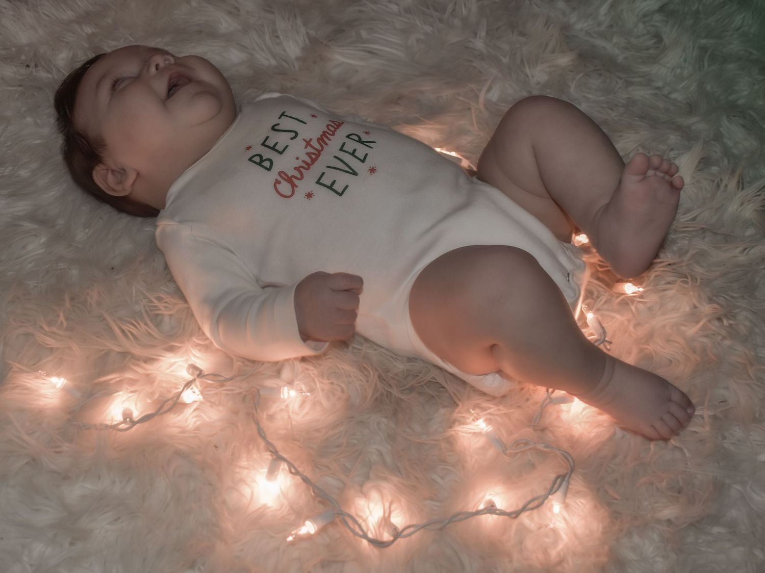 Baby lying on soft blanket with glowing string lights creating a dreamy holiday atmosphere.