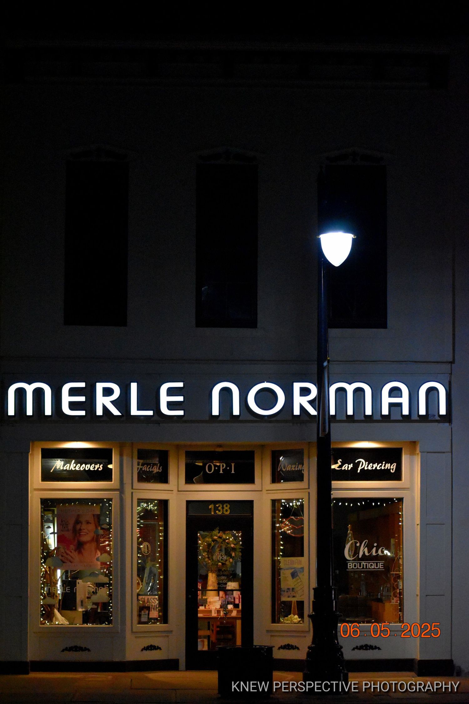 Illuminated Merle Norman storefront at night with glowing signage and window displays.
