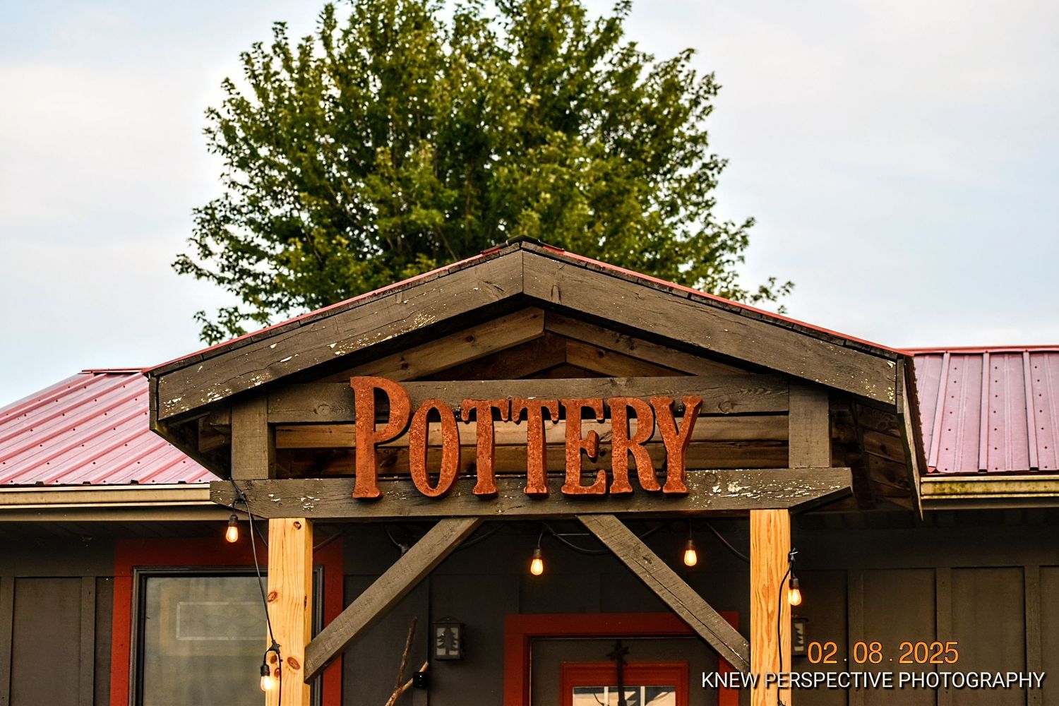 A rustic wooden sign reading 'Pottery' hangs above the entrance of a building with a metal roof.