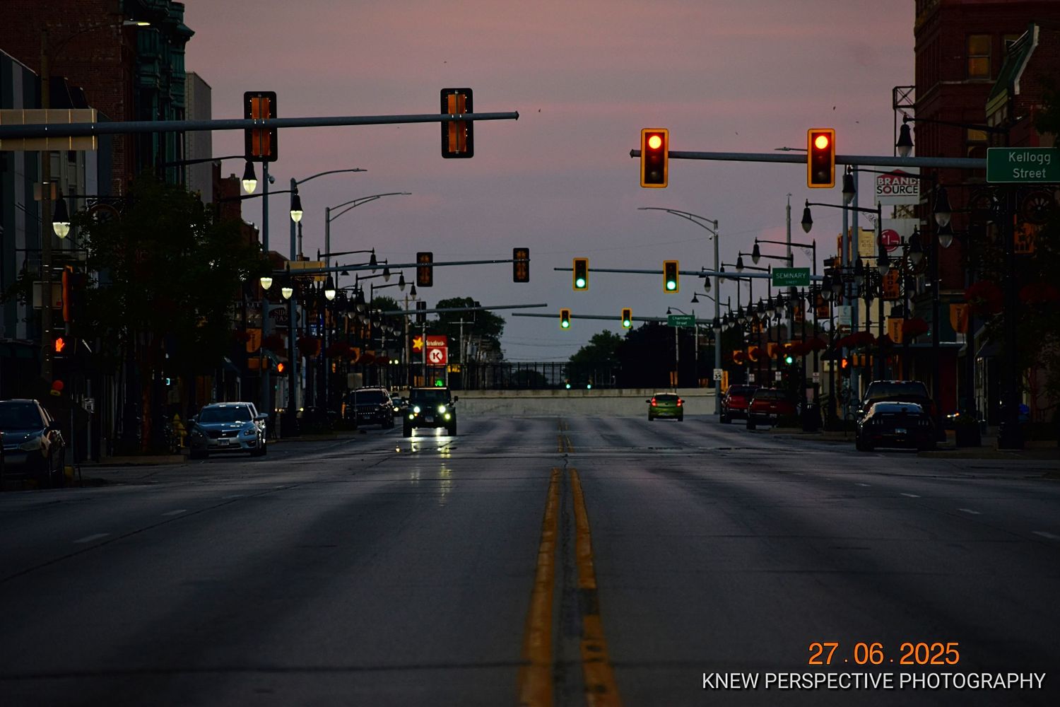 A panoramic view of empty city streets at dusk with traffic lights glowing against a purple-pink sky.