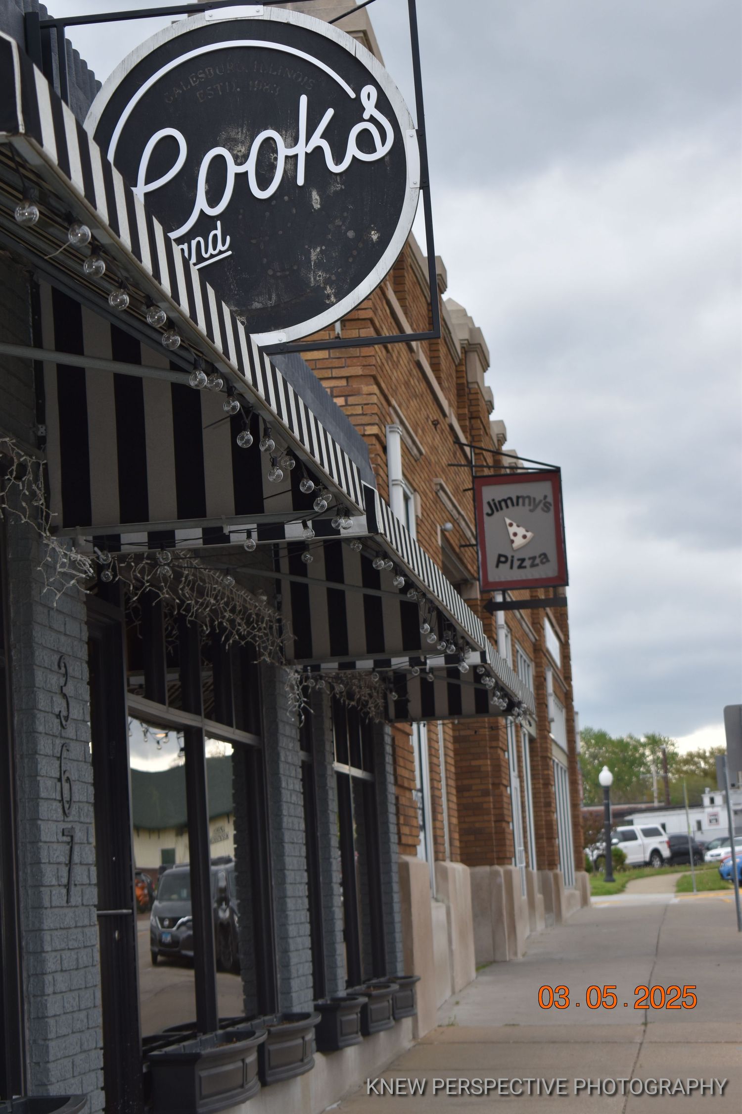 Exterior view of a storefront with black and white striped awnings and signage on a cloudy day.