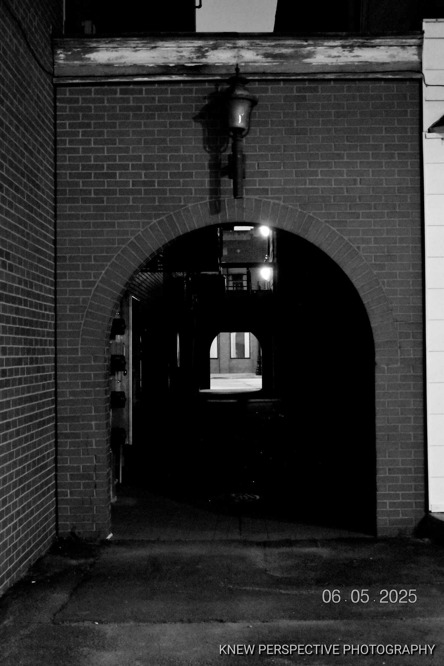 A dark tunnel-like passageway with brick walls and arched entrances shown in a black and white photo.