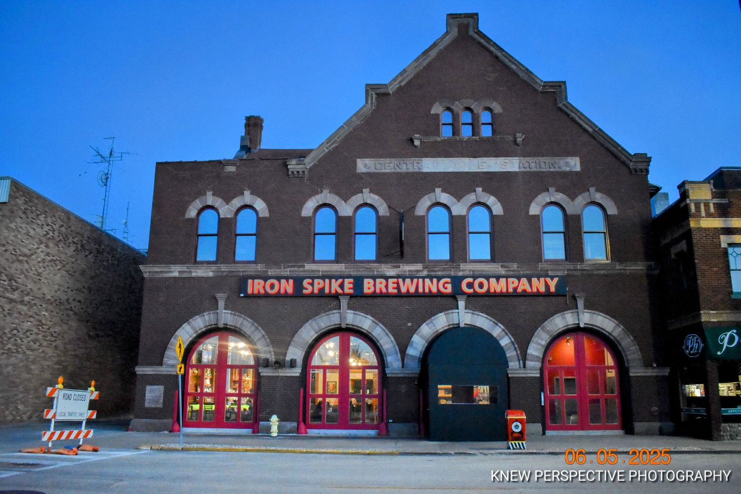 Historic brick building with arched windows illuminated at night showcases Iron Spike Brewing Company's exterior facade.