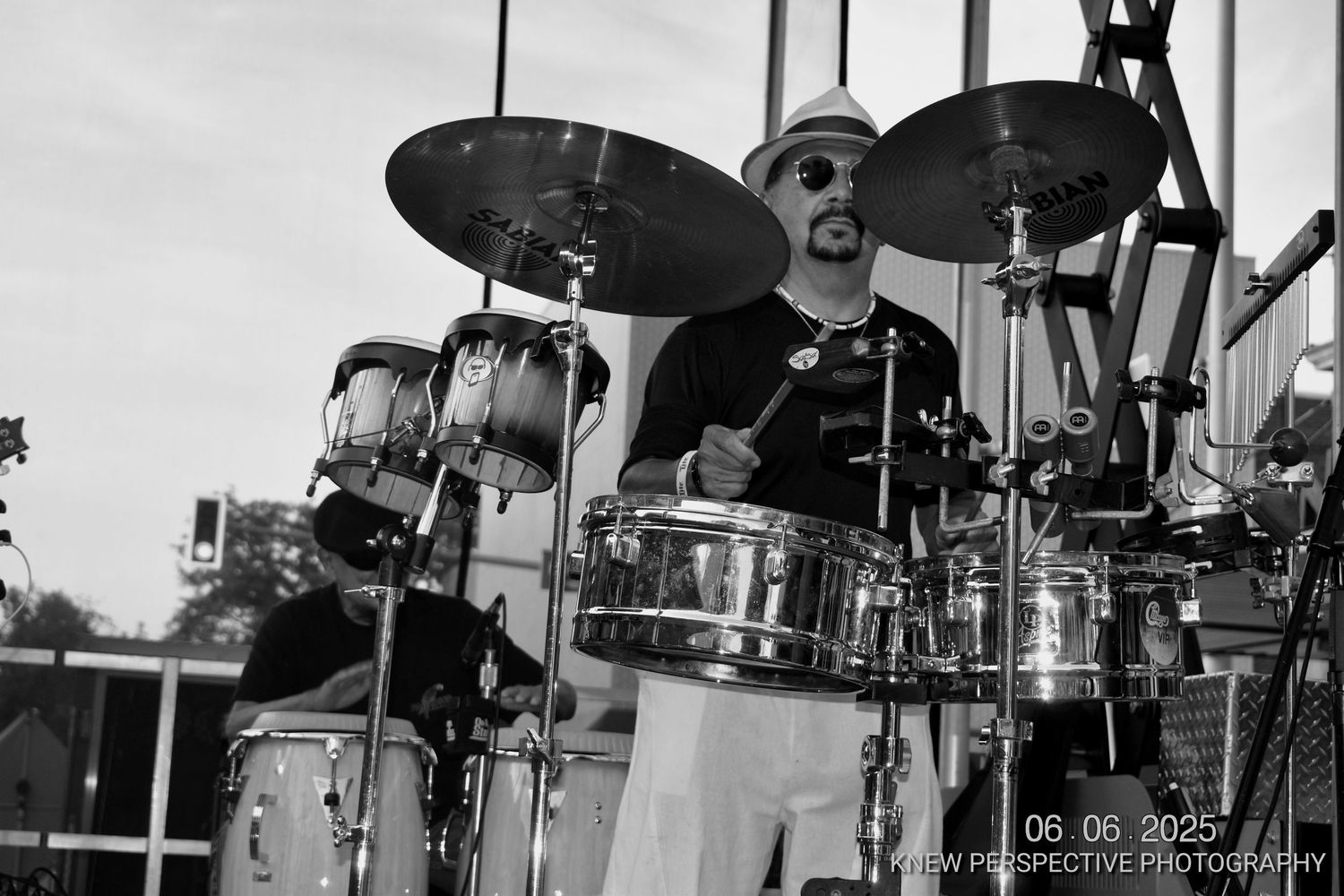 Black and white photo of a drummer performing on stage with multiple drum sets and cymbals visible.
