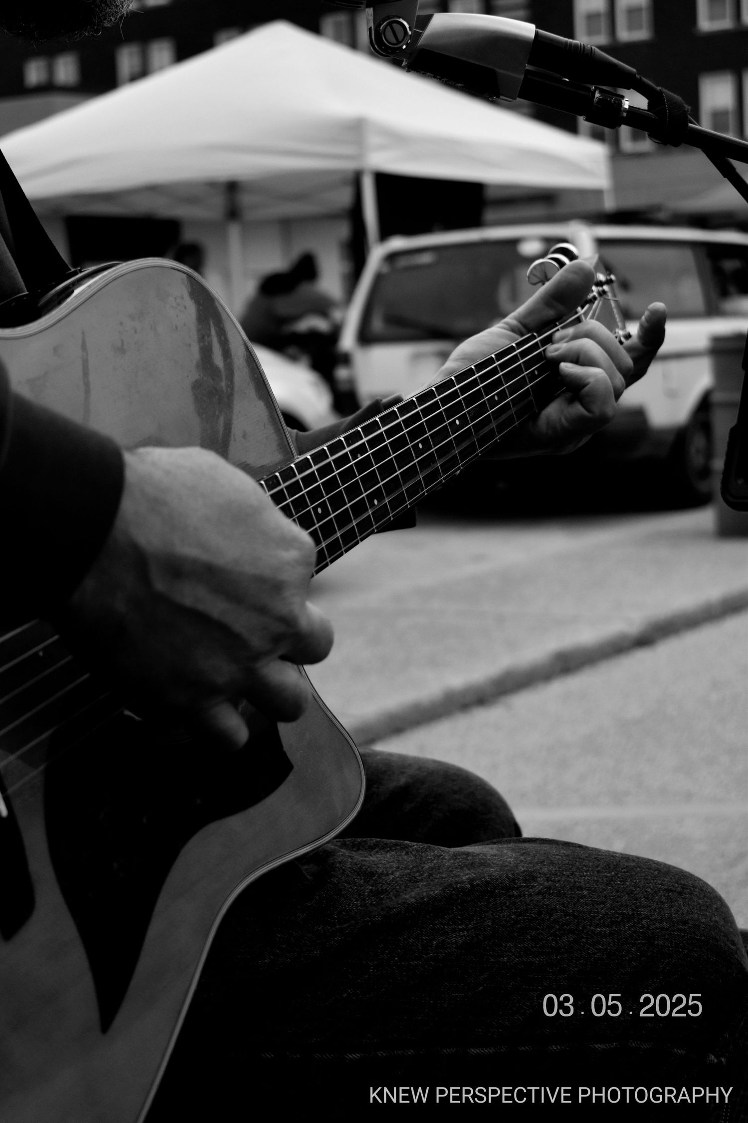 Close-up black and white sequence of hands playing acoustic guitar strings in an outdoor setting.