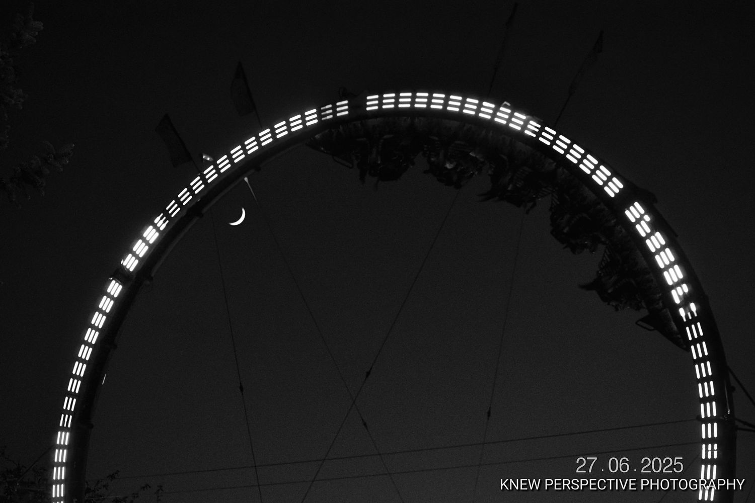 A series of lights on a carnival ride arranged in an arc pattern against a dark background creates a minimalist geometric design in b&w