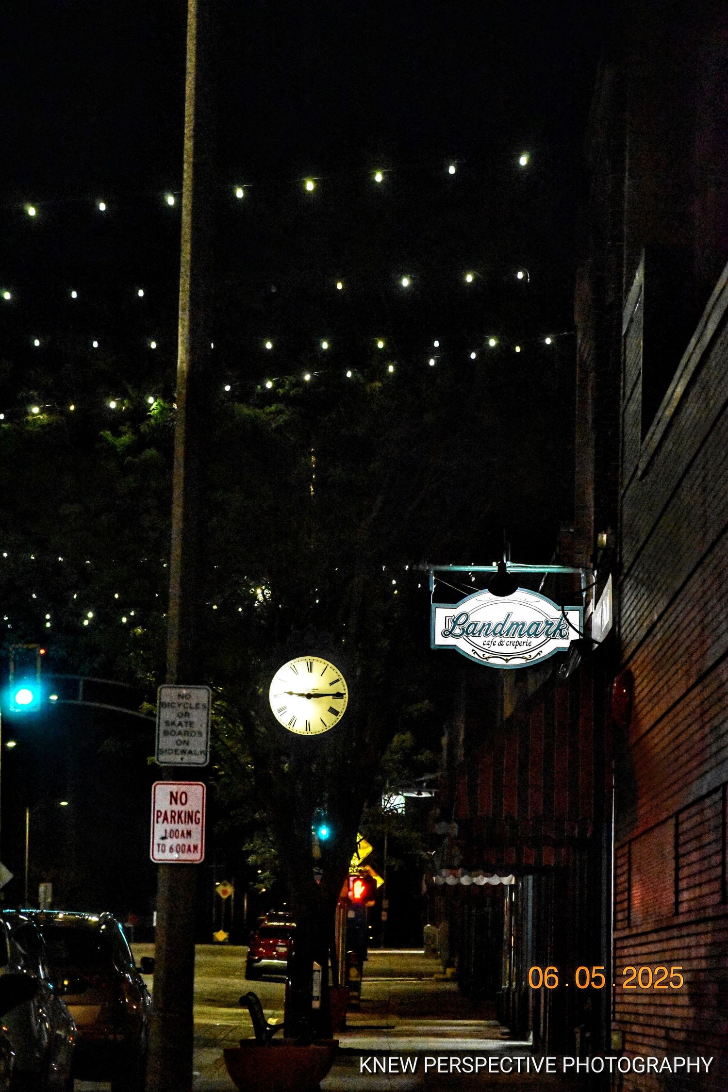 String lights illuminate a dark street scene with a clock and business signs visible at night.