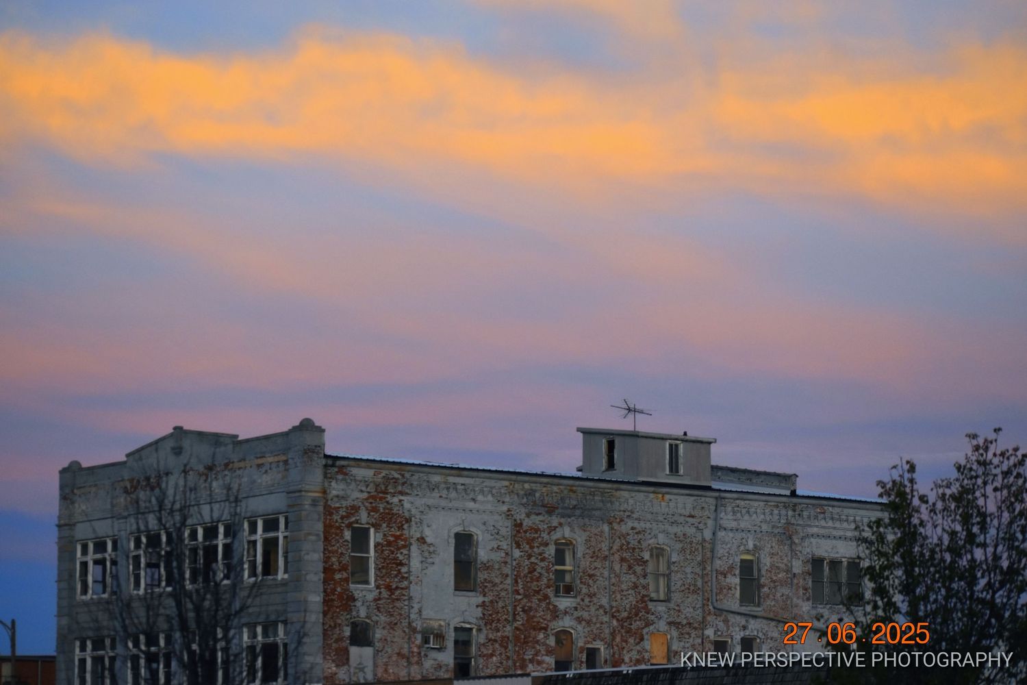 Panoramic cityscape silhouette against a vibrant orange and purple sunset sky with clouds reflecting warm light.