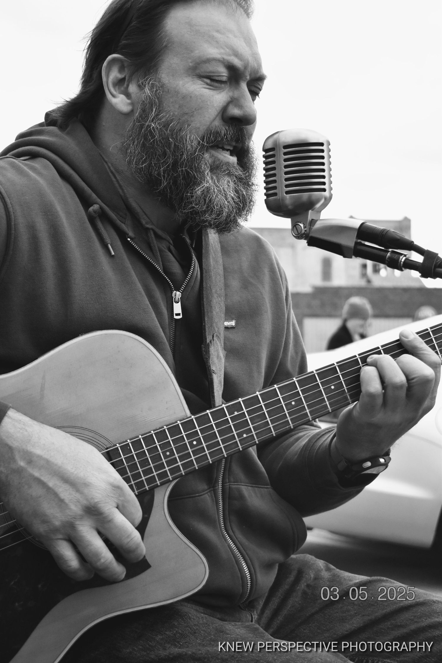 Black and white photo sequence showing musician playing acoustic guitar and singing into vintage microphone during performance.