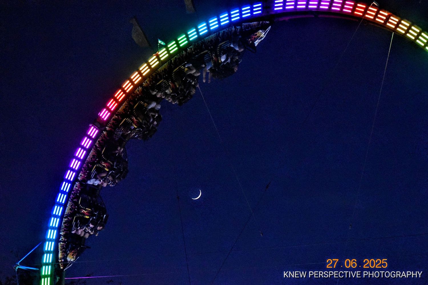 Colorful LED lights illuminate a curved carnival ride against a dark night sky creating a vibrant rainbow effect.