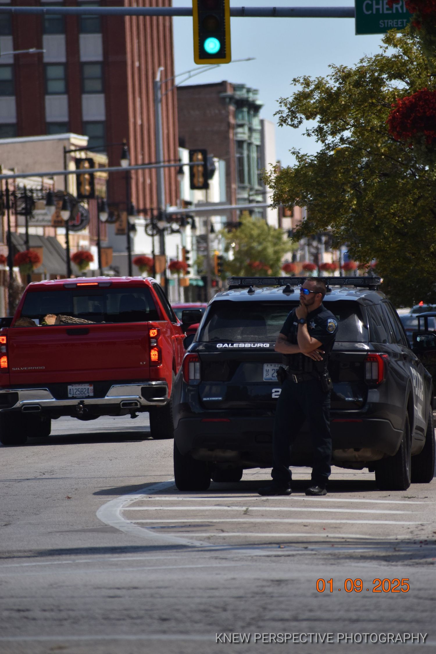 Police Officer ans squad car on an urban street with traffic lights and buildings visible in the background.