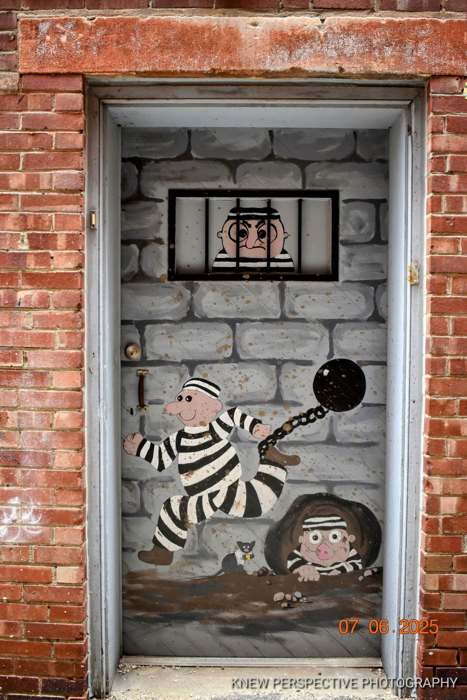 Street art mural sequence shows a prisoner in striped outfit breaking free with ball and chain in brick doorways.
