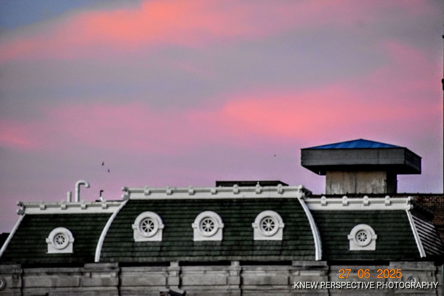 A panoramic view of industrial buildings silhouetted against a vibrant pink and purple sunset sky.
