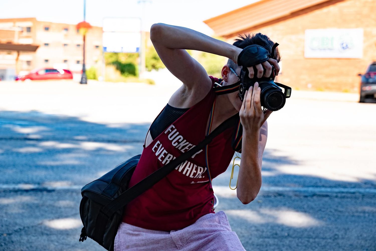 A photographer in a crimson tank top takes a photo outdoors on a sunny day.