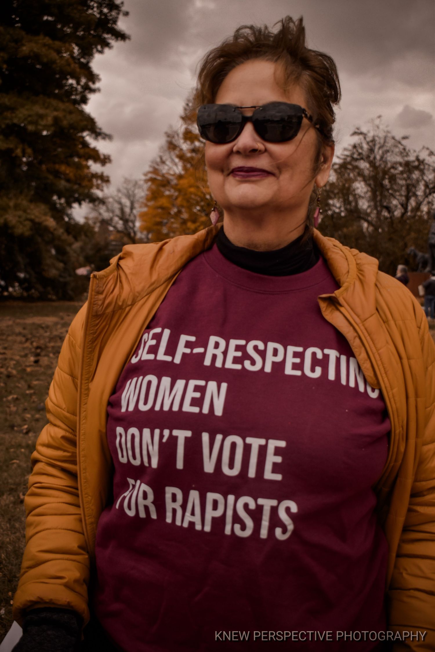 photo showing a burgundy t-shirt with protest text 'self-respecting women don't vote for rapists' against a moody autumn background.