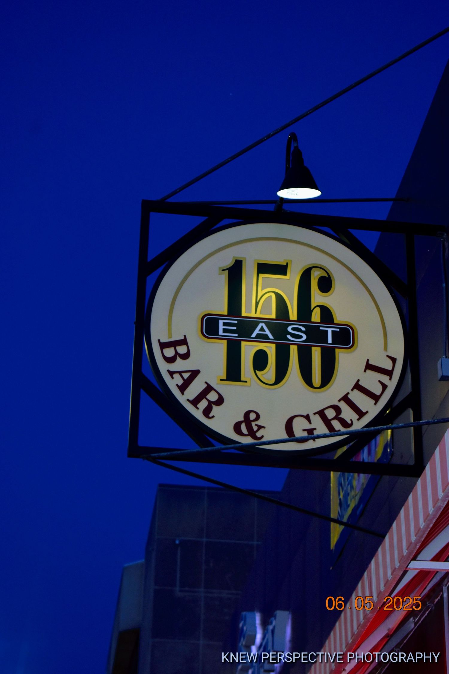 Illuminated vintage business sign for 156 East Bar & Grill against a deep blue twilight sky.