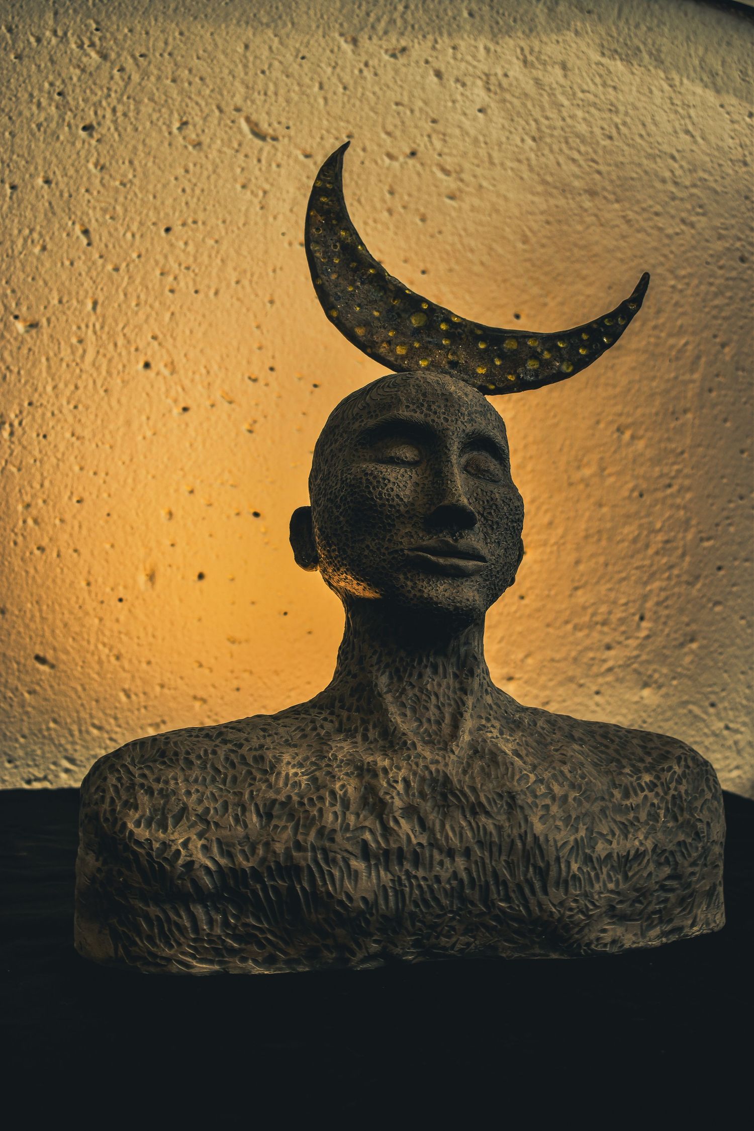 Silhouetted sculpture with crescent moon shapes against an amber lit textured background.