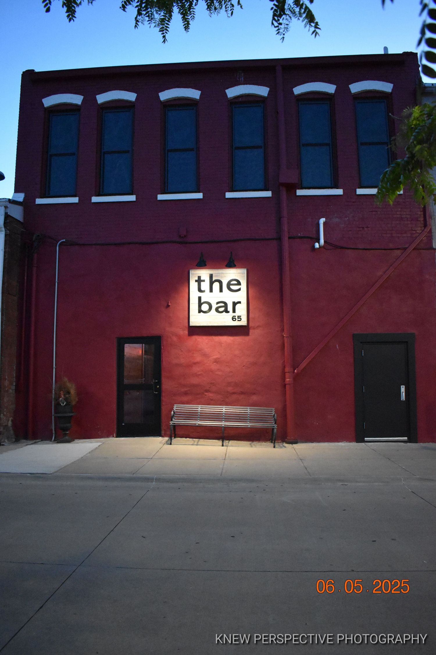 Panoramic view of a red brick building exterior with 'the bar 65' signage and multiple windows at dusk.