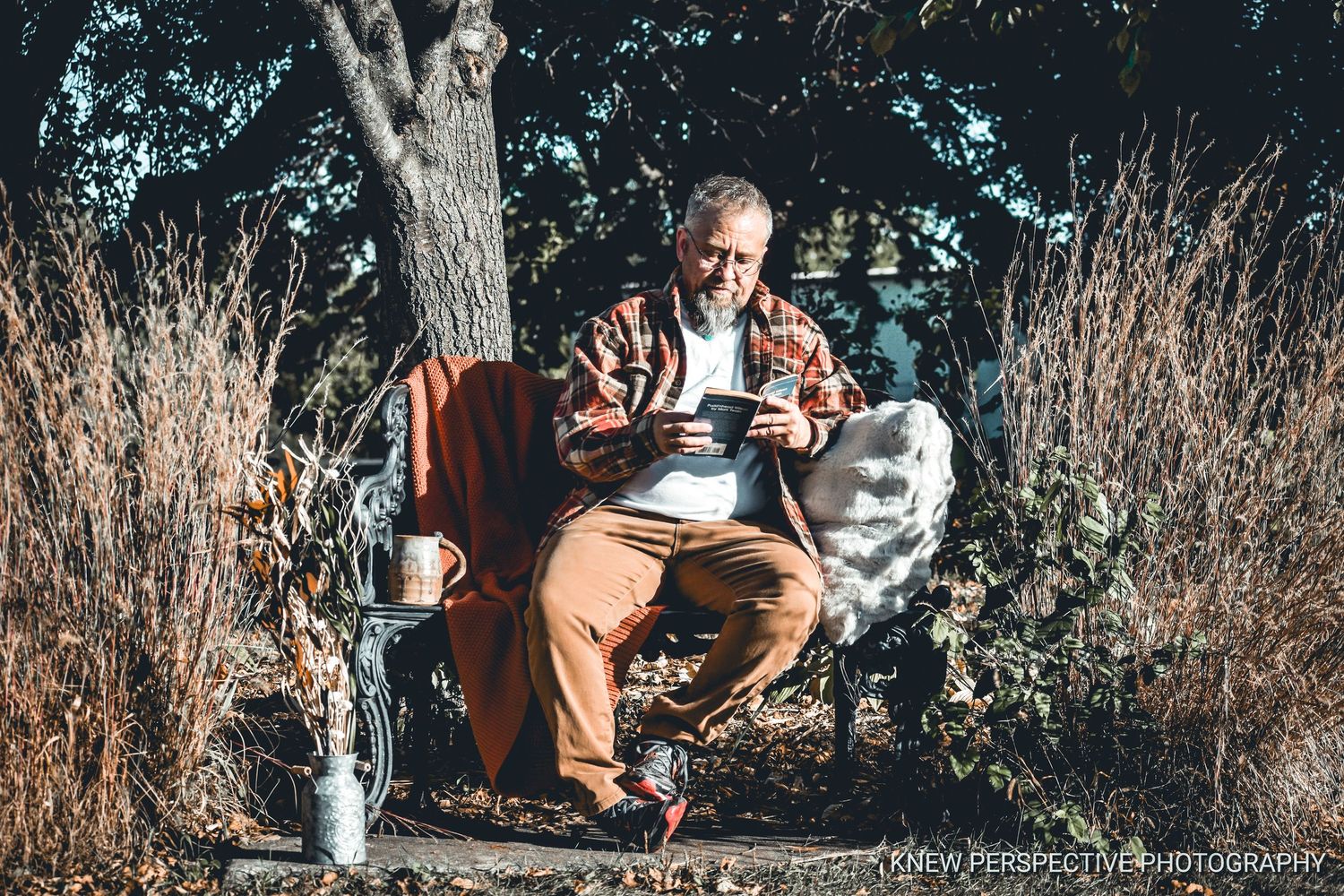 Someone sits in a white metal bench outdoors in nature while reading, with a mug nearby.
