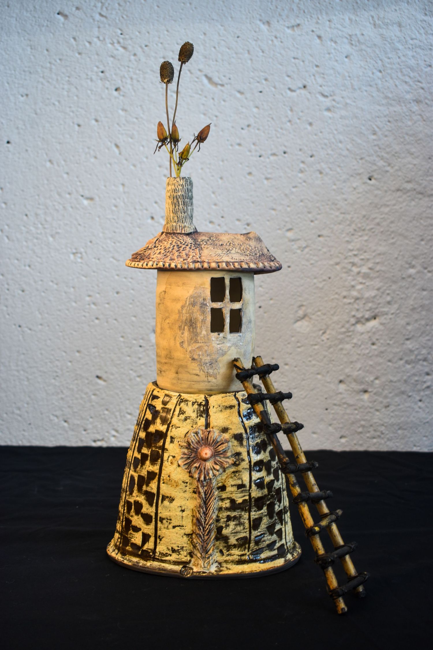 Artistic ceramic sculpture resembling a rustic tower with ladder and floral motifs captured from multiple angles.