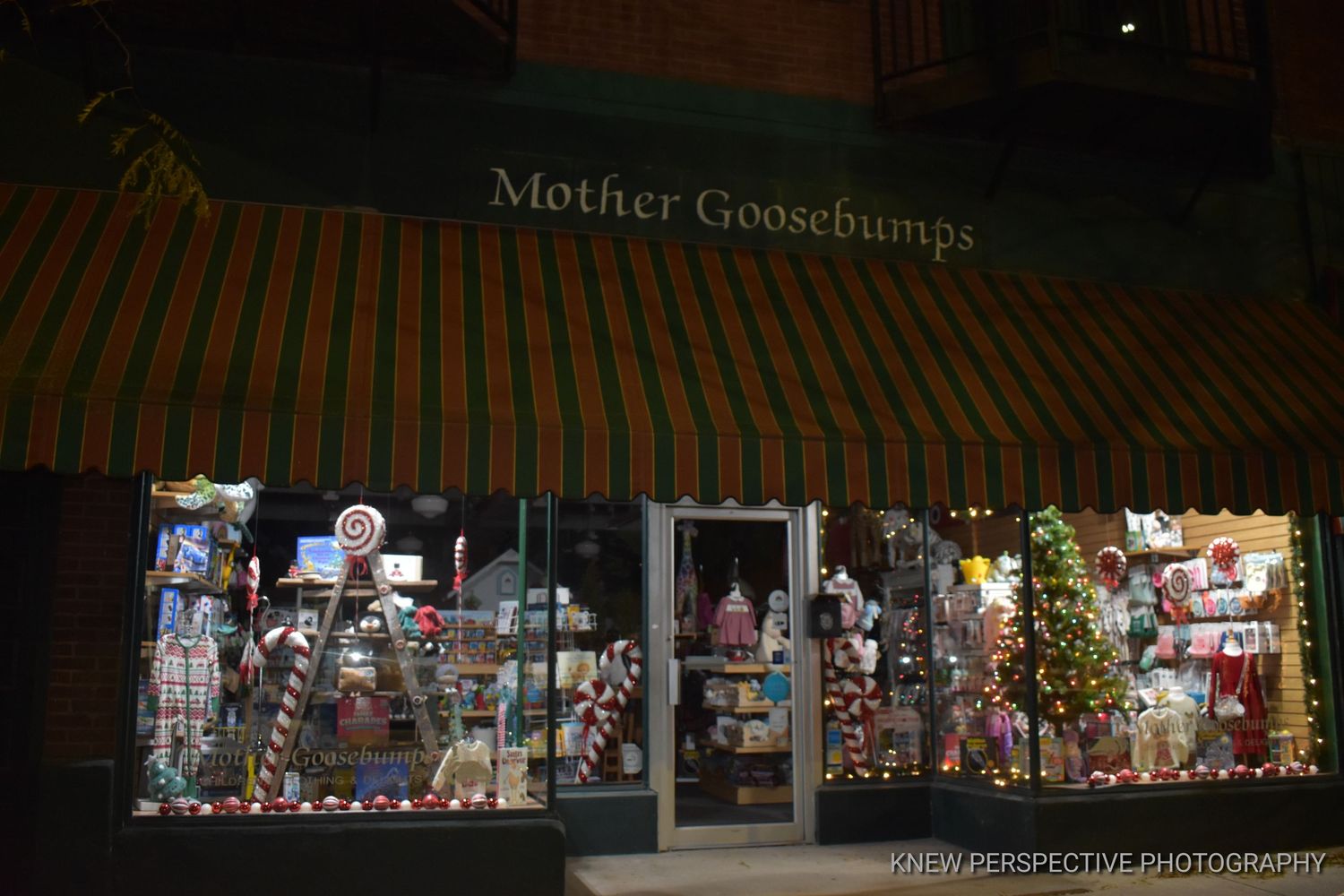 A storefront window display at night illuminated with Christmas lights and decorations showing a festive holiday scene.