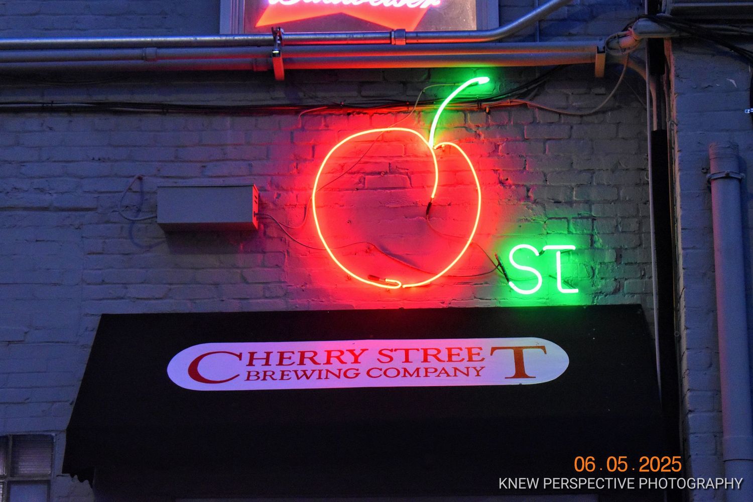 Neon signs illuminate the exterior of Cherry Street Brewing Company at night with red and green glowing lights.