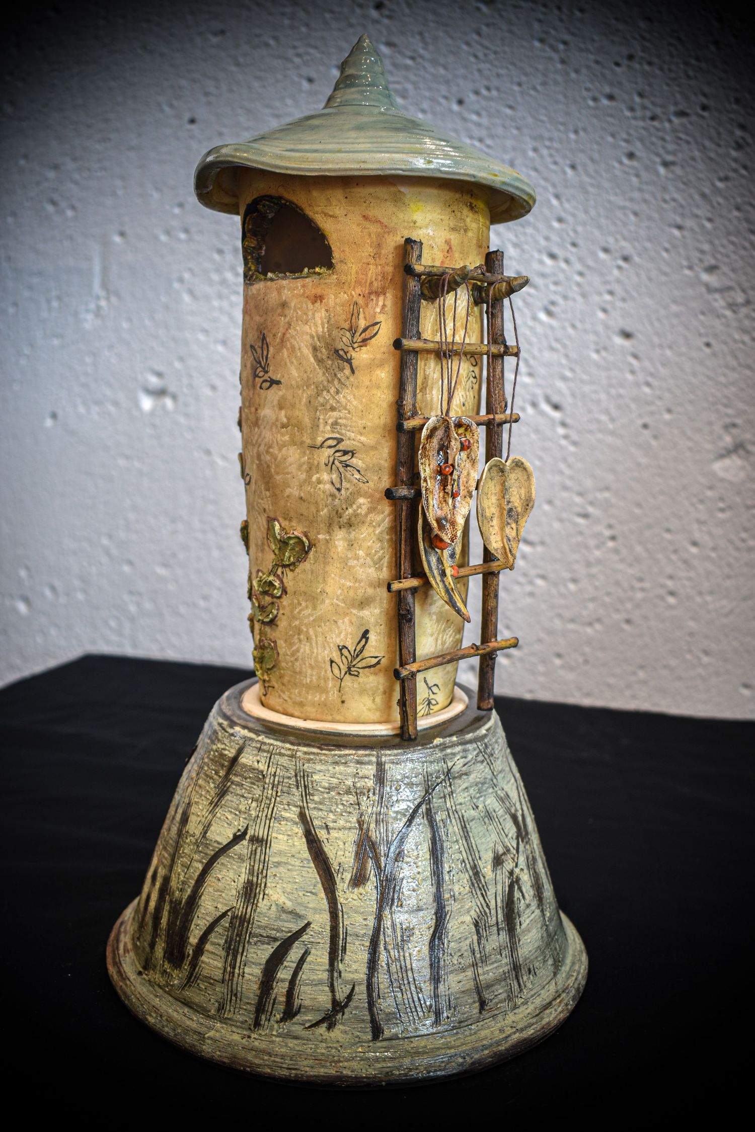 Handcrafted ceramic tower sculpture with textured details, bamboo ladder, and decorative base featuring nature motifs.