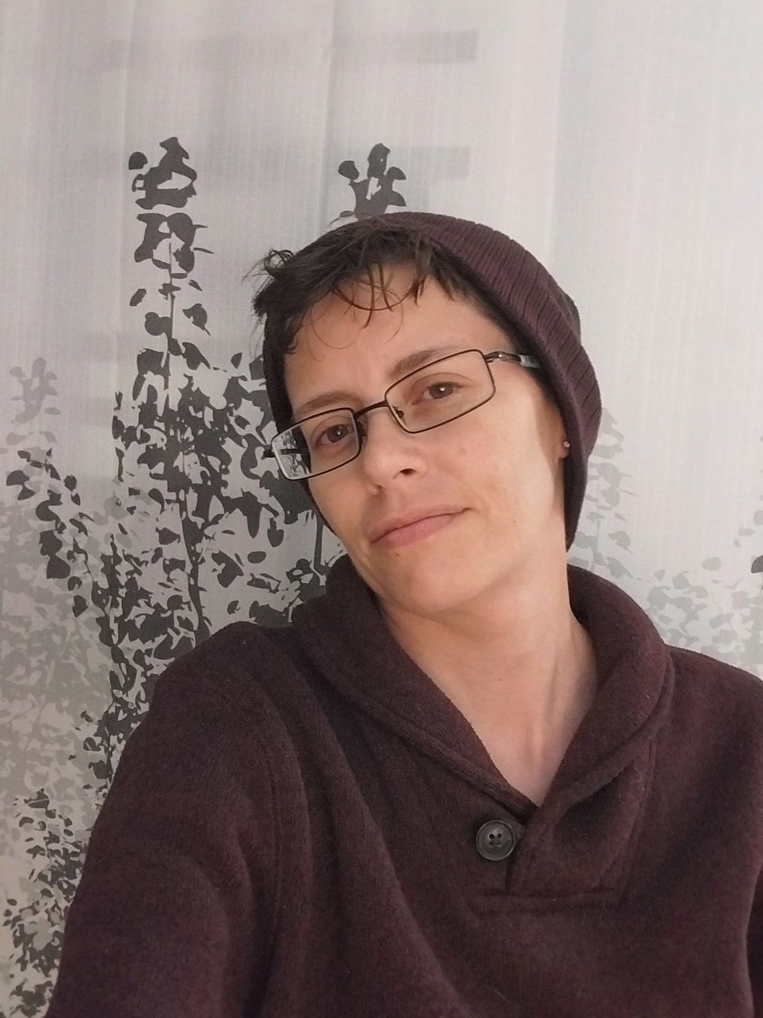 A person wearing glasses and a burgundy sweater poses in a casual selfie series against a light background.