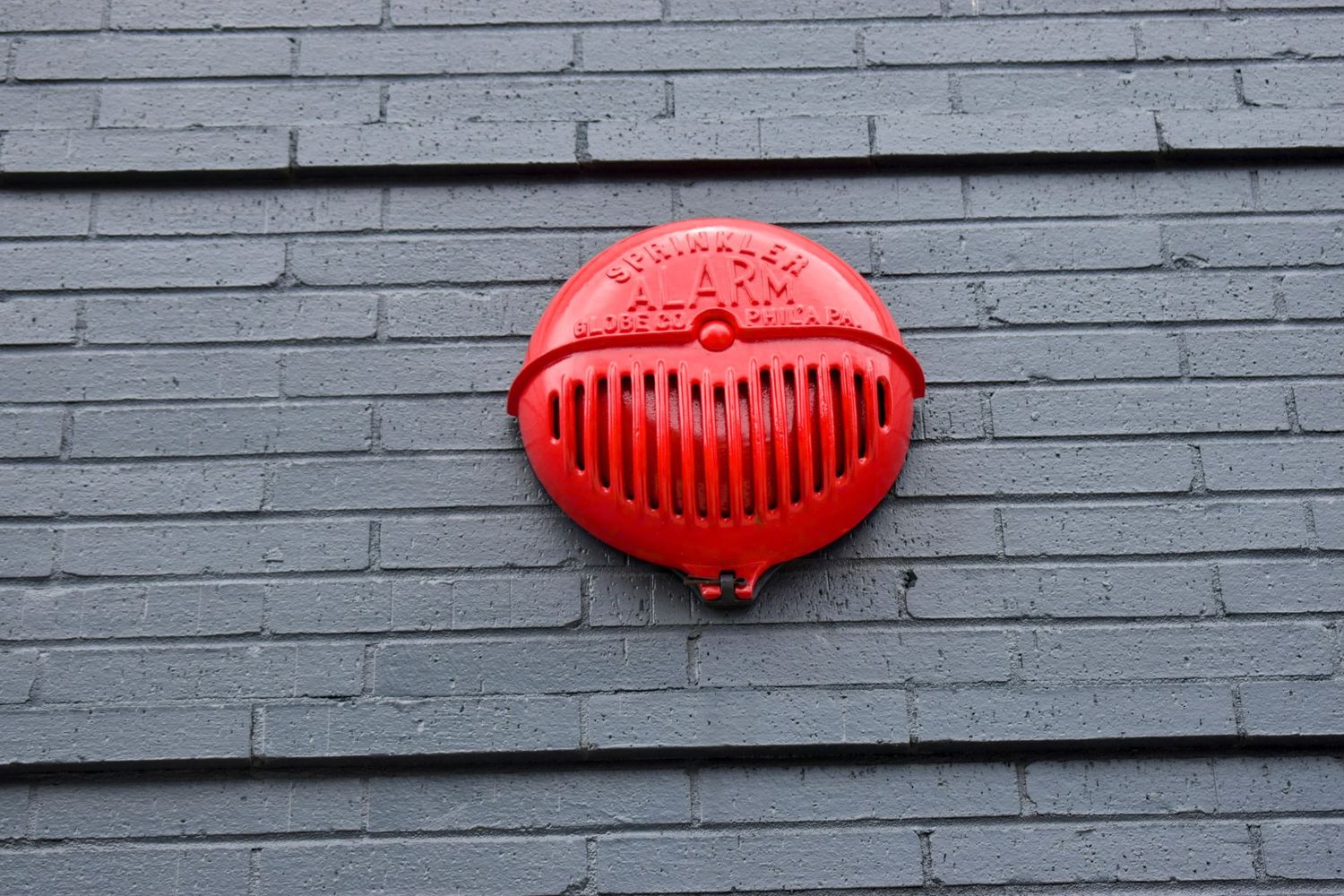 A bright red vintage-style fire alarm mounted on a gray brick wall.