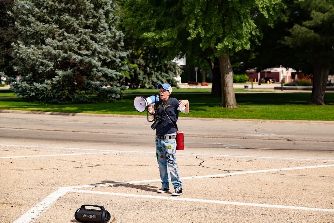 A photographer carrying camera equipment speaking to a crowd with a megaphone