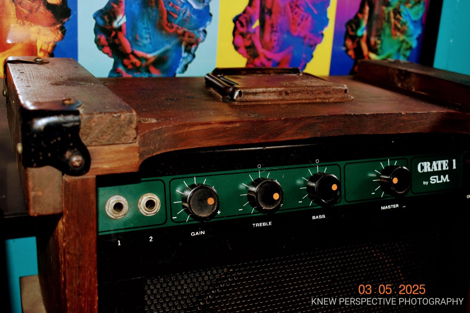 Close-up view of a vintage guitar amplifier with green control panel against colorful pop art background.