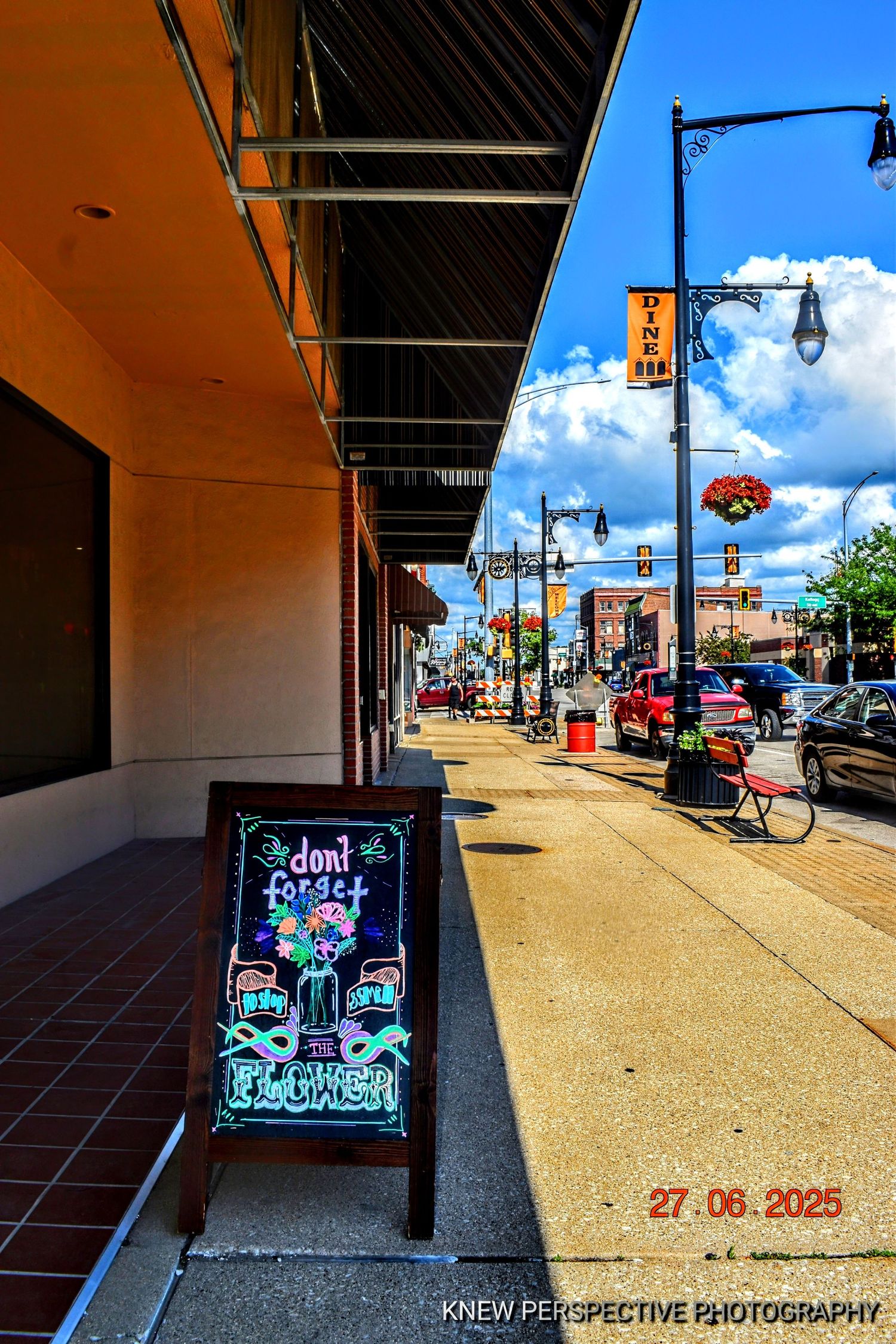 A panoramic view of a storefront sidewalk with signs and street lamps under bright blue skies in a small town.
