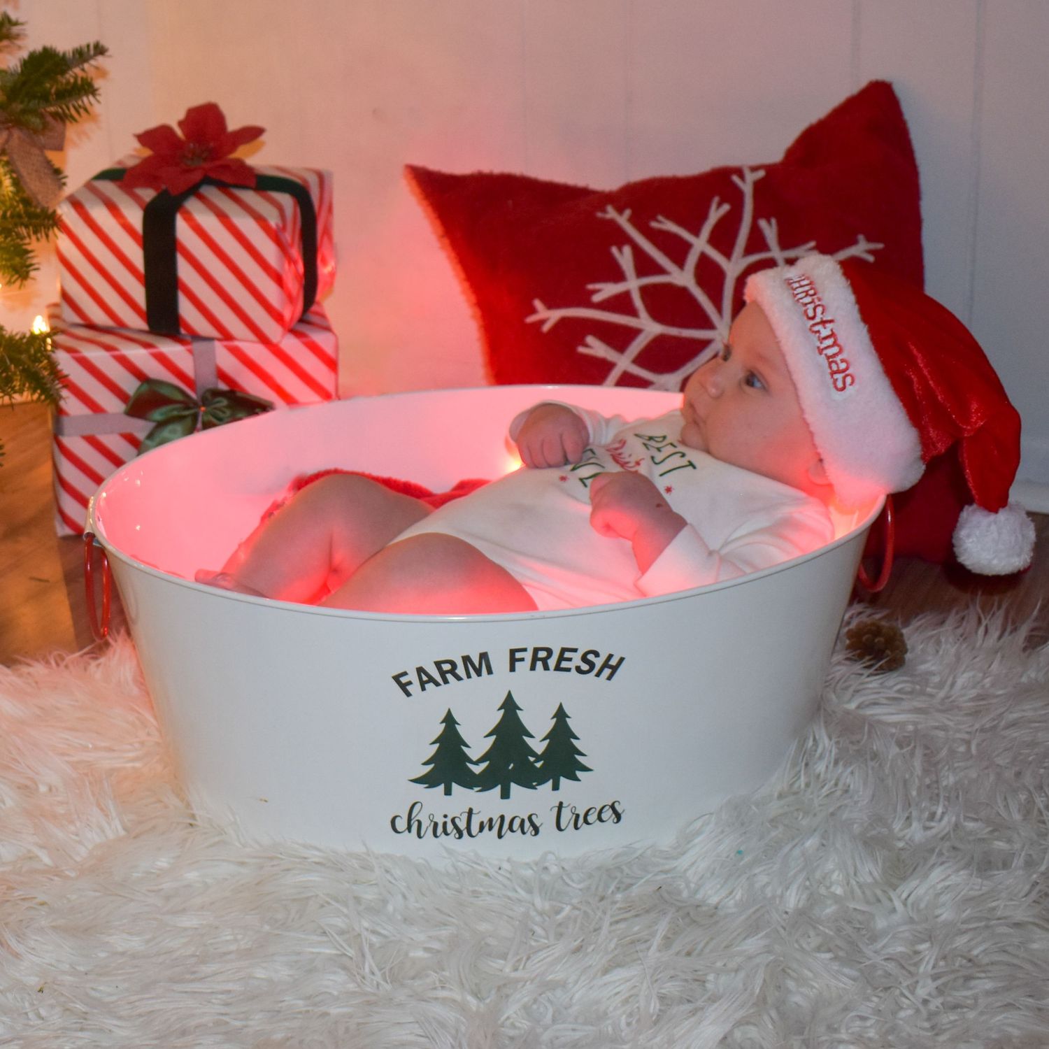 A festive Christmas scene with a baby in a red Santa hat, and glowing red lights creating a cozy holiday atmosphere.