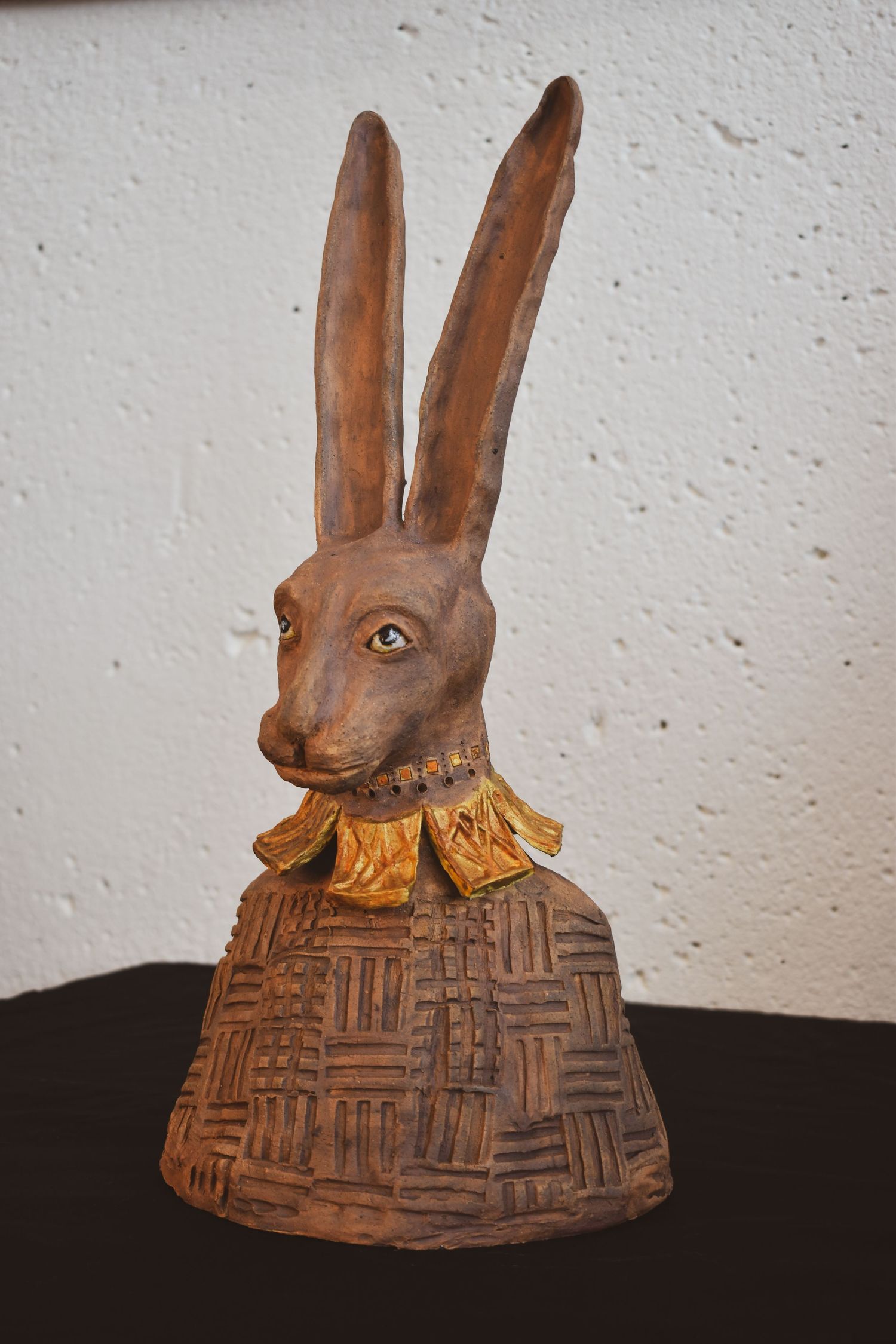A clay carved rabbit head sculpture with intricate geometric patterns on its base.