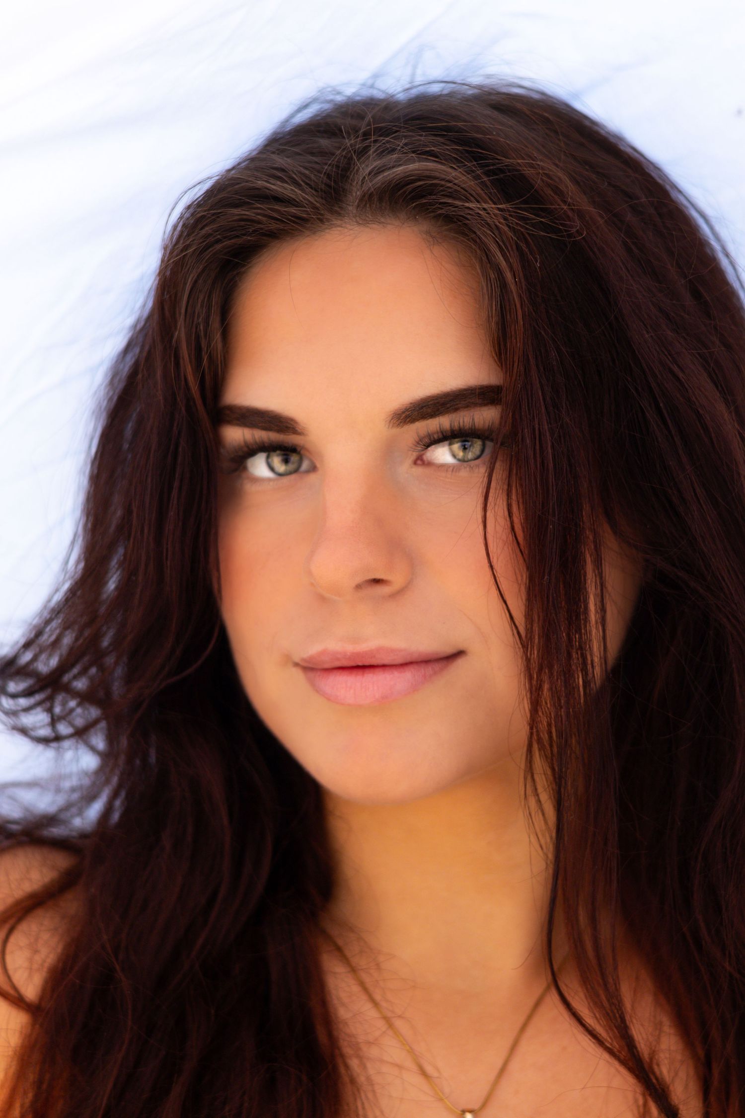 Beautiful young woman with long dark hair and green eyes posing against a white background outdoors.