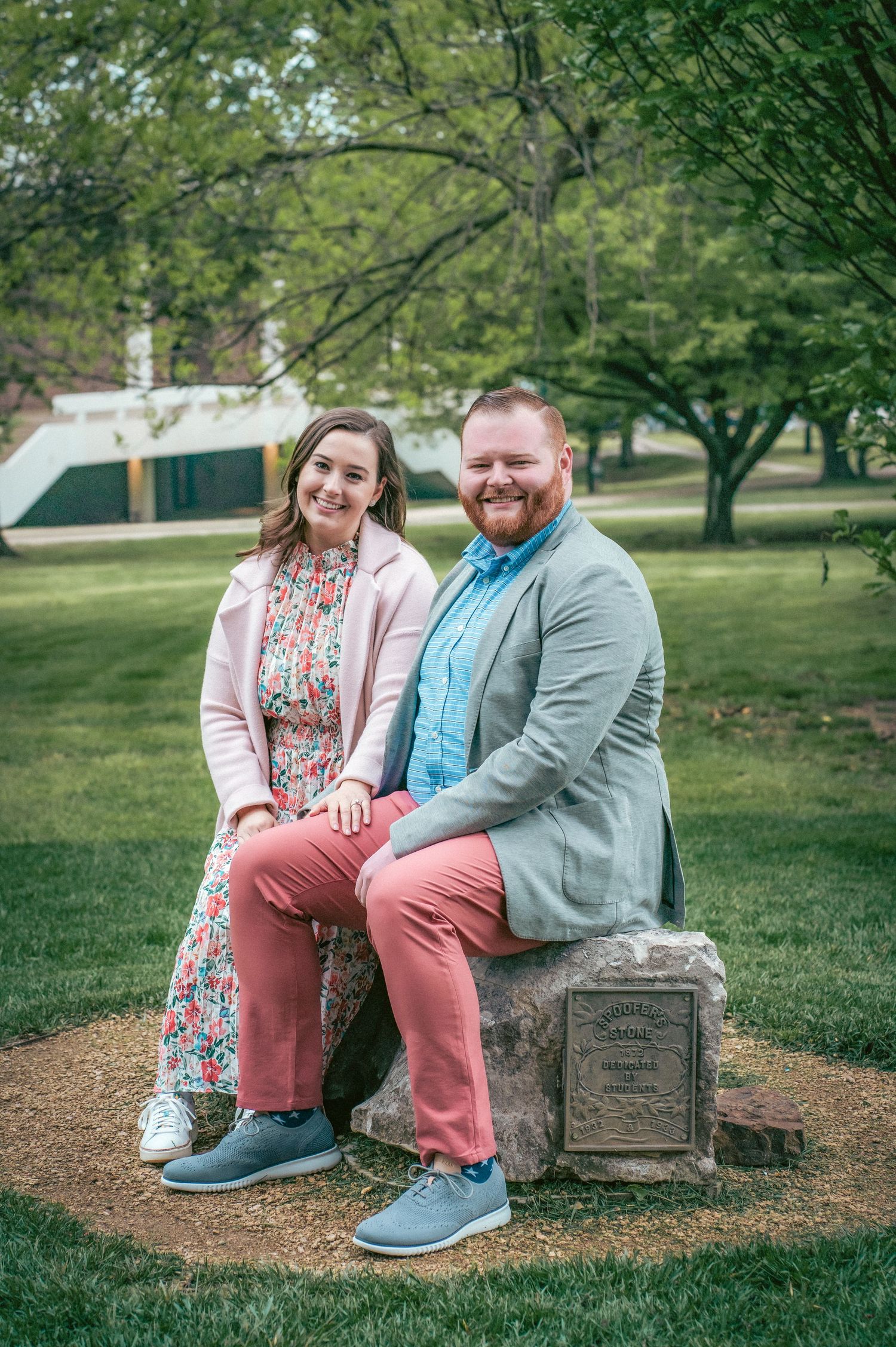 Couple sits together on stone marker in park setting.