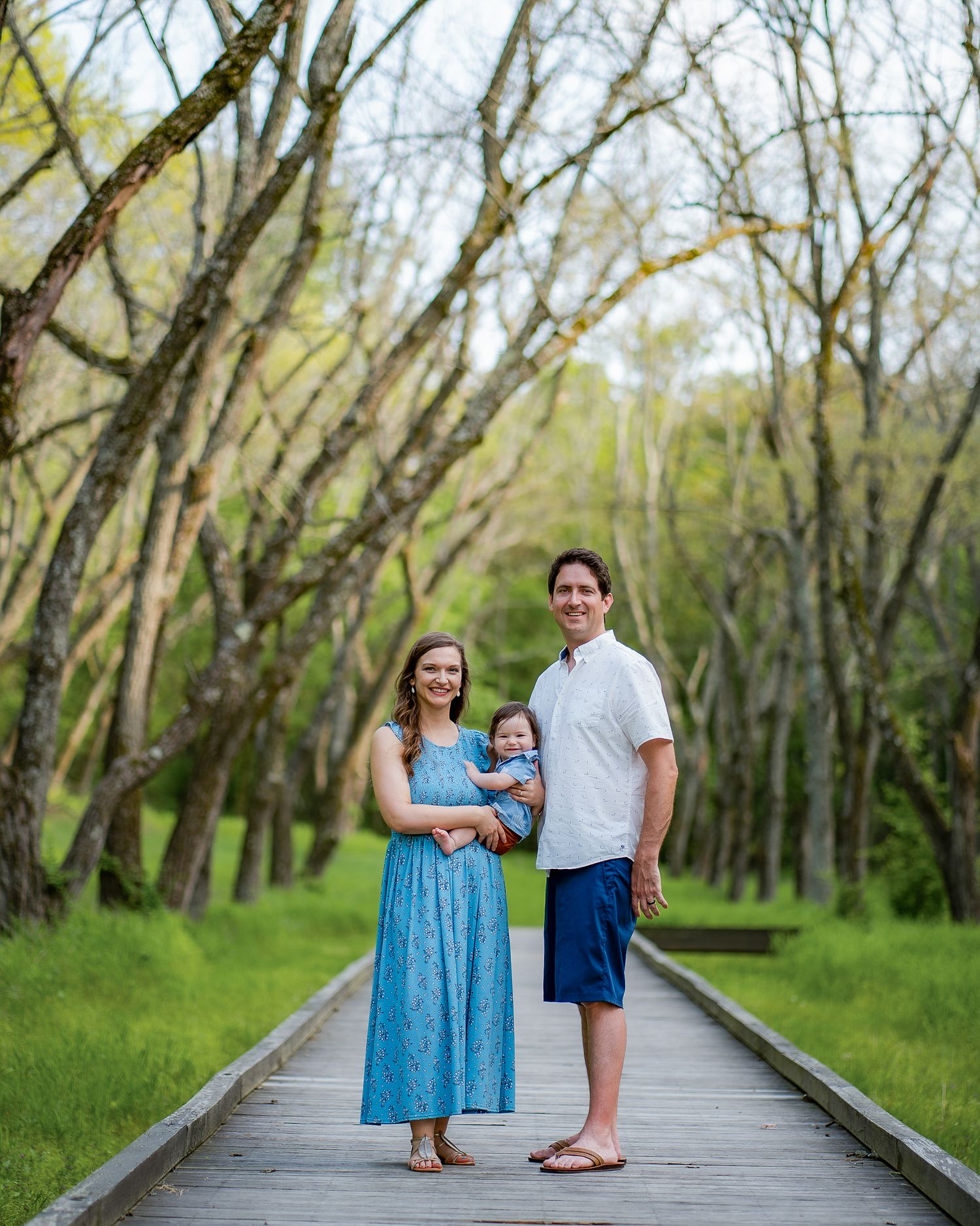 A family standing on a wooden boardwalk surrounded by spring trees in a natural setting.