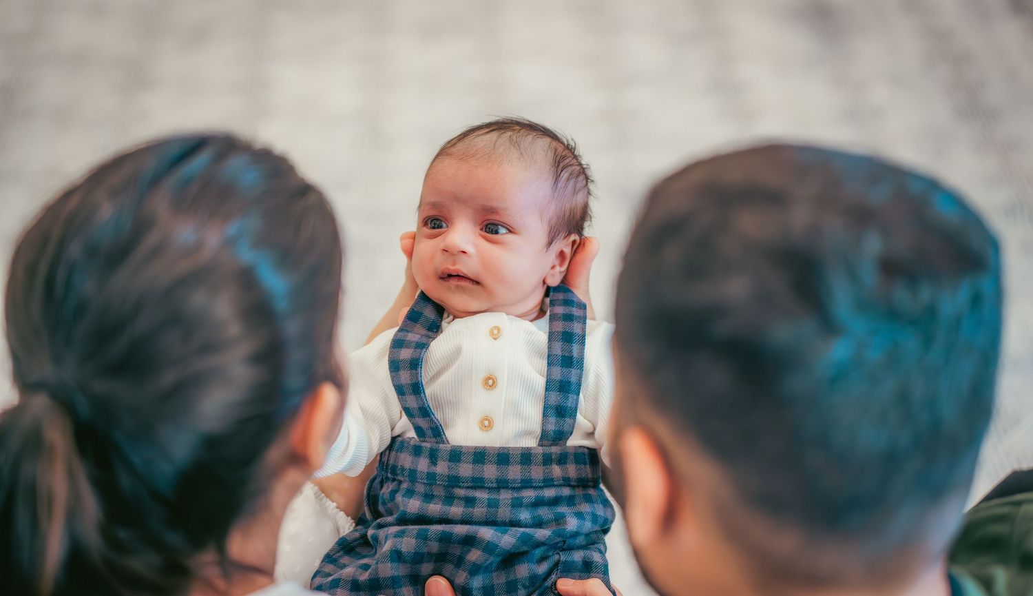 Close up portrait of an infant wearing plaid overalls.