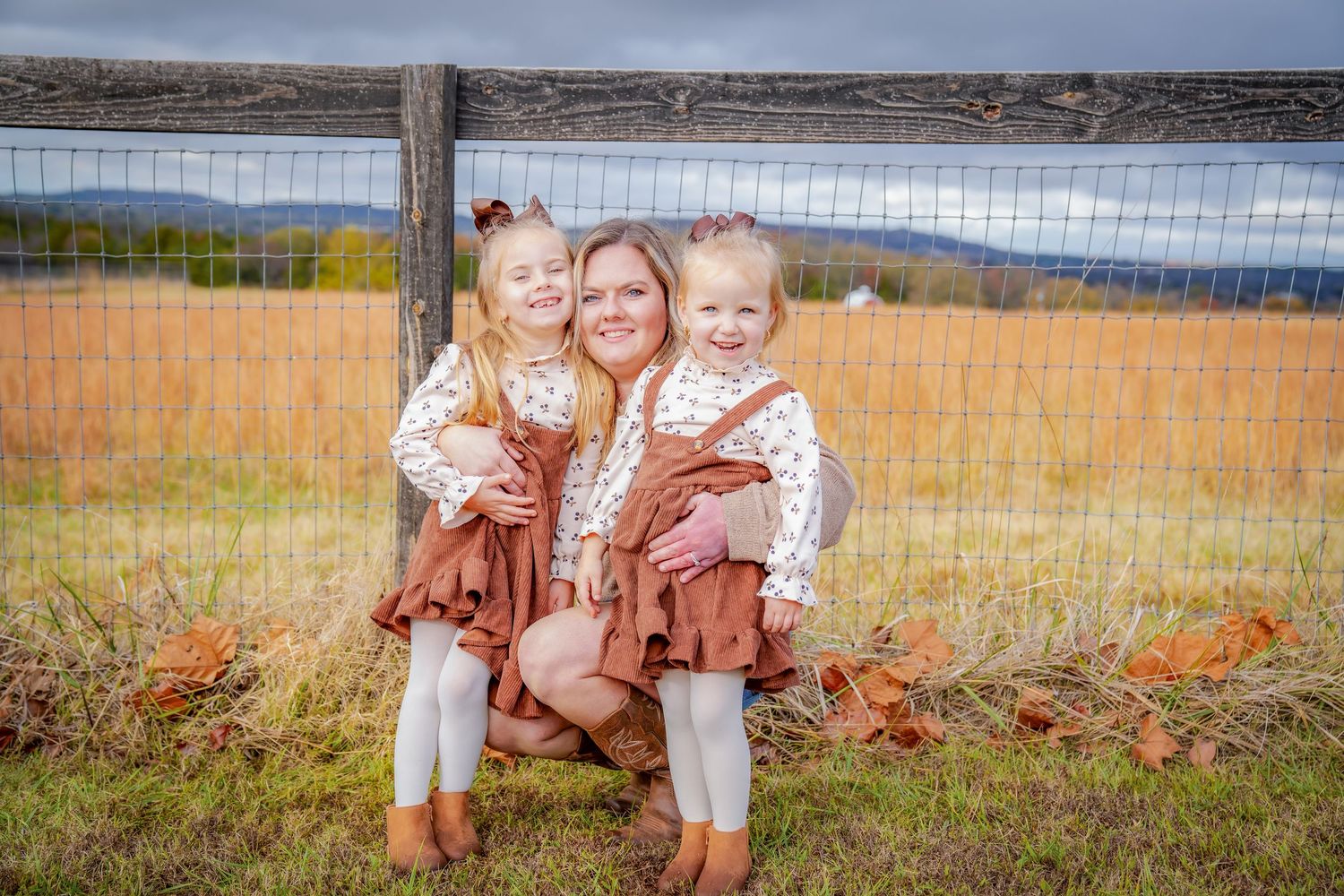 Family poses together in coordinated outfits near rustic fence during fall season.