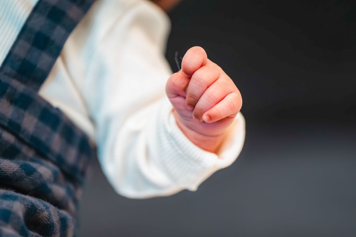 Close up of tiny baby fingers against dark background.