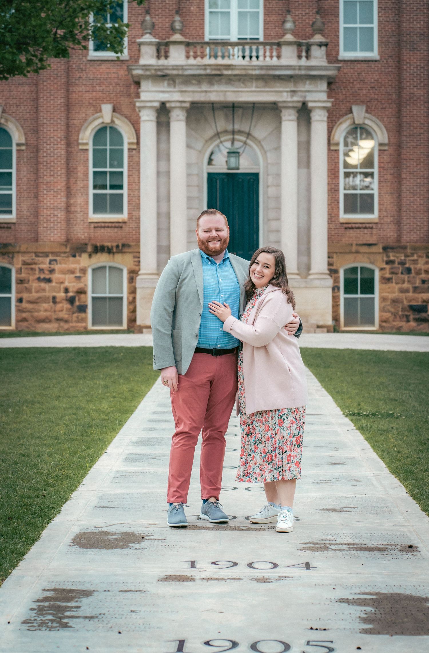 Playful couple posing on vintage stone walkway with historic brick building in background.
