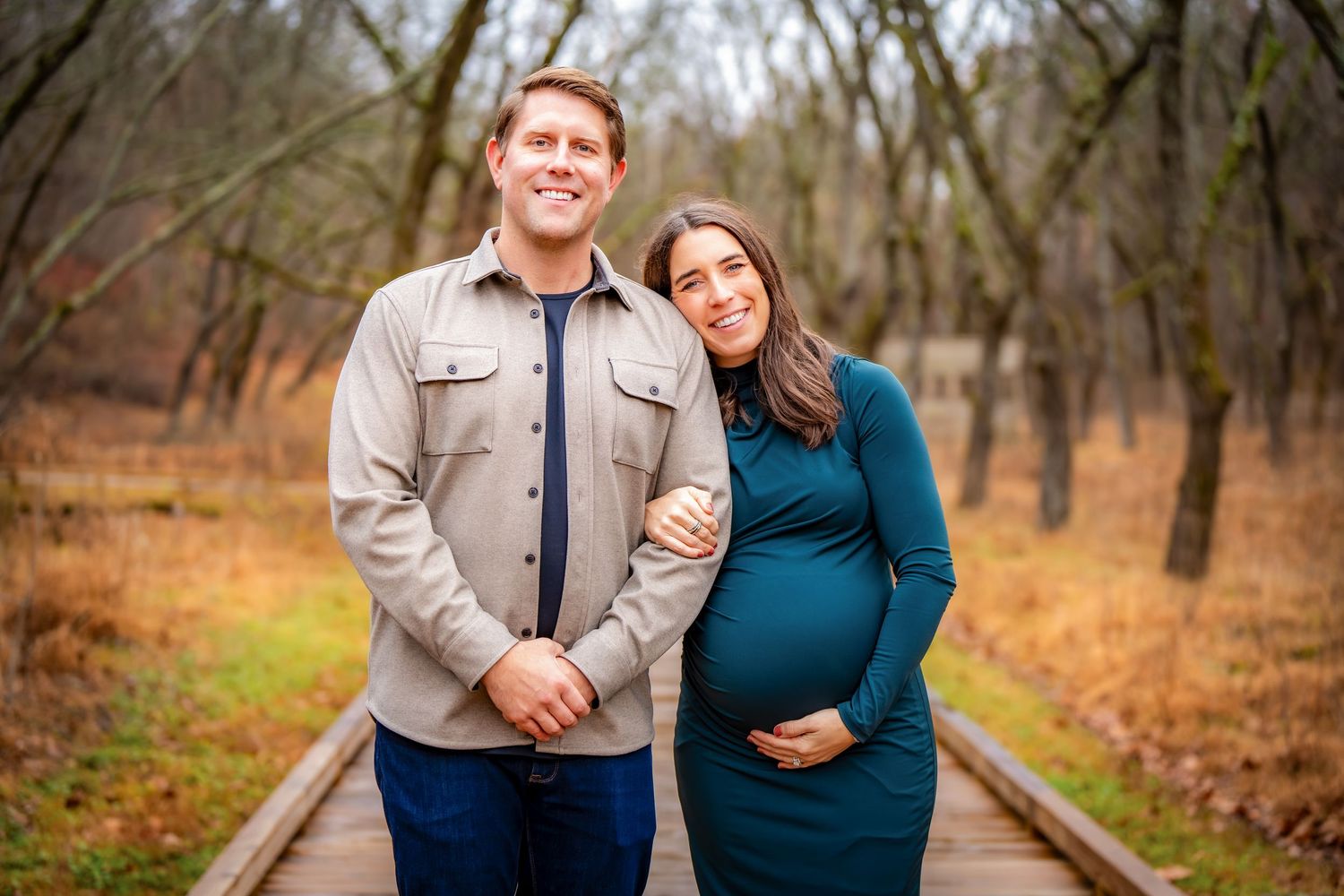 A couple shares intimate moments while walking along a wooden path through autumn woods.