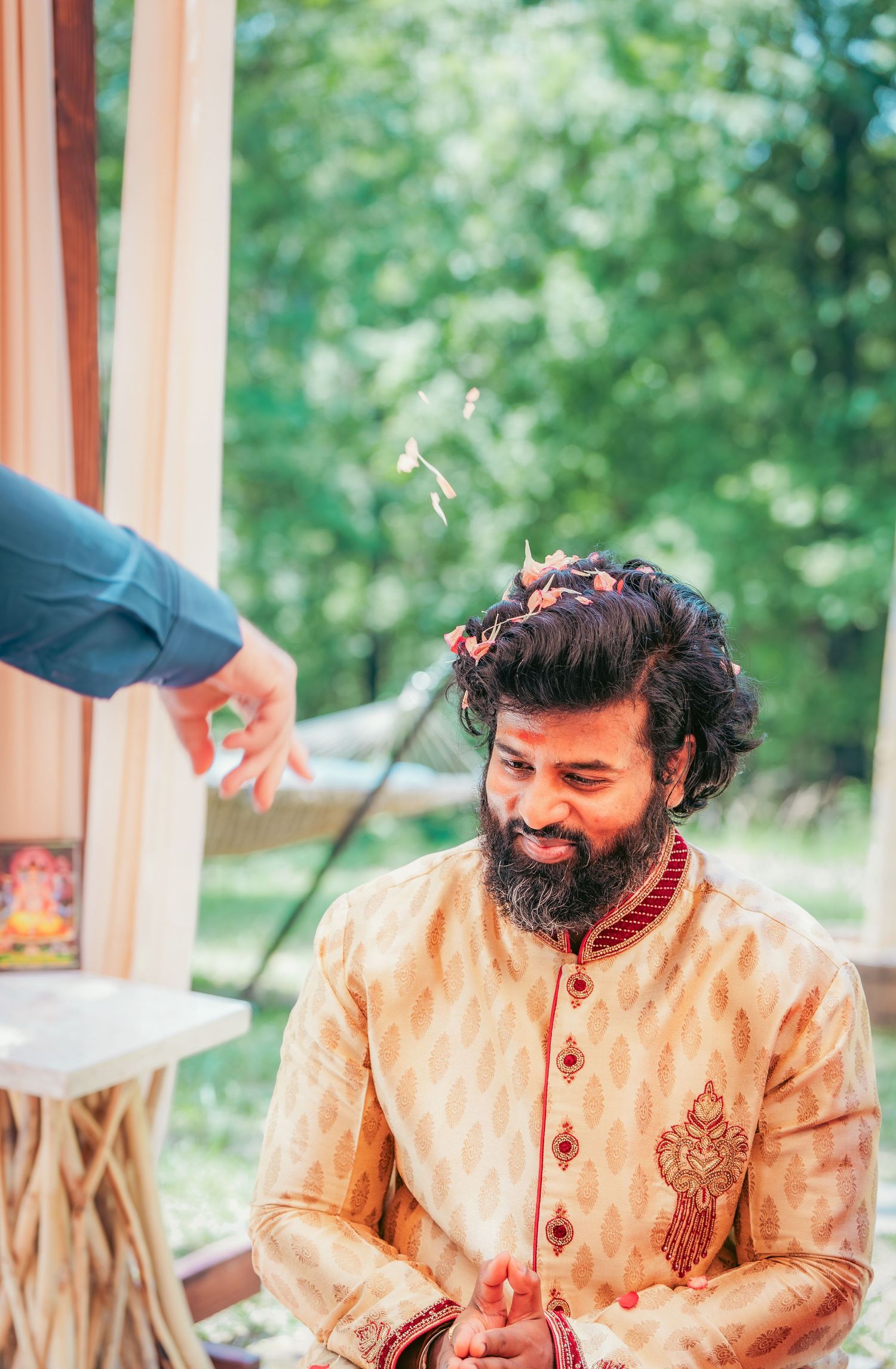 Person in cream-colored traditional Indian wedding attire laughing during ceremony.