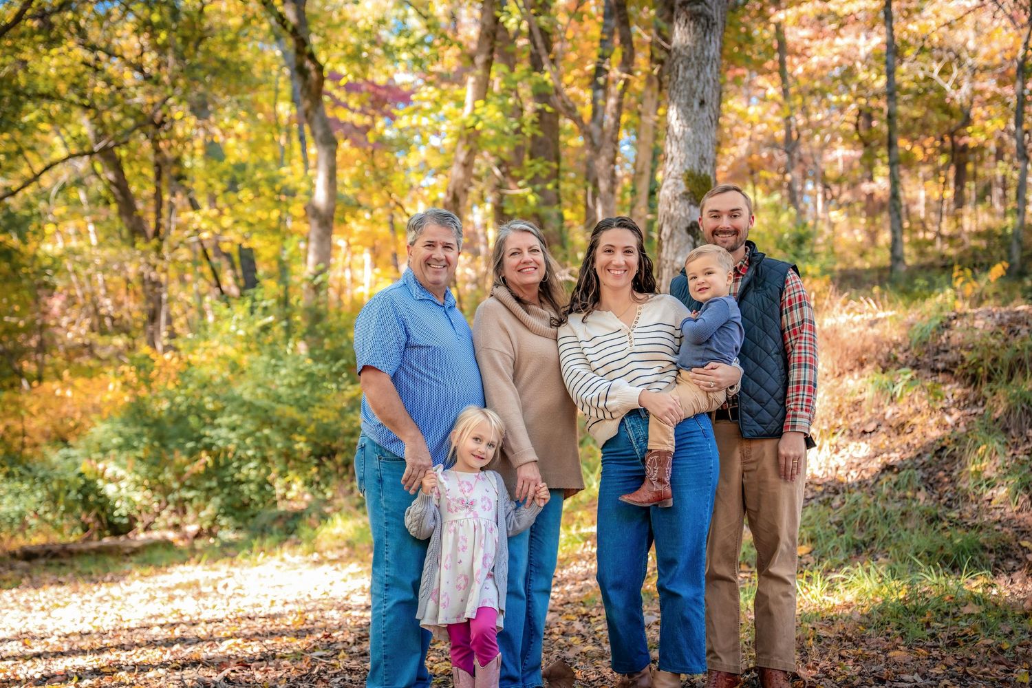 Family gathering outdoors among fall foliage and trees in casual attire.