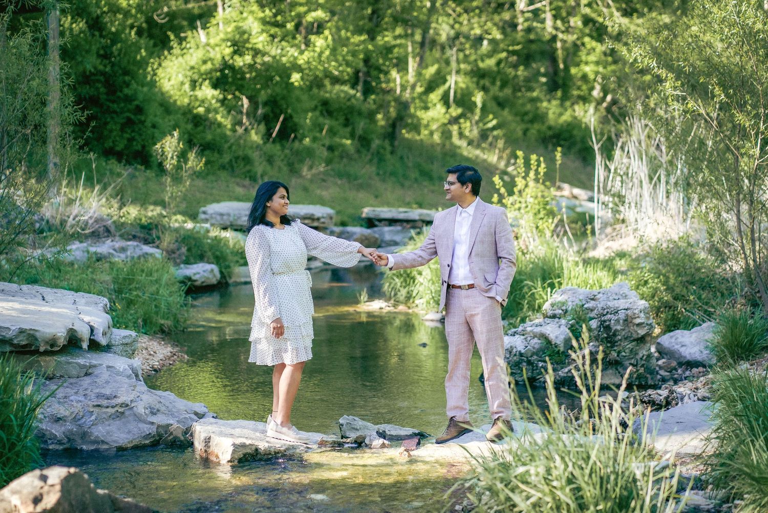 A couple enjoys a romantic moment by a peaceful stream surrounded by natural scenery.