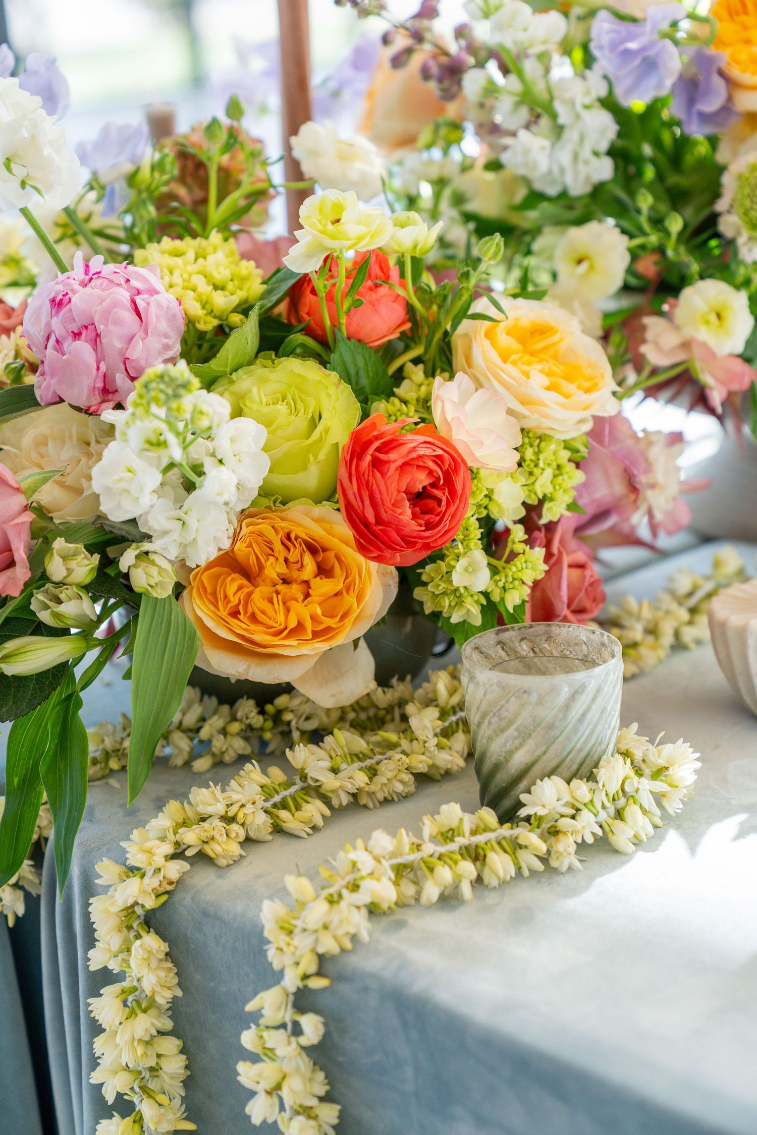 Colorful spring flower arrangements with roses and hydrangeas in gray vases on white tablecloth.