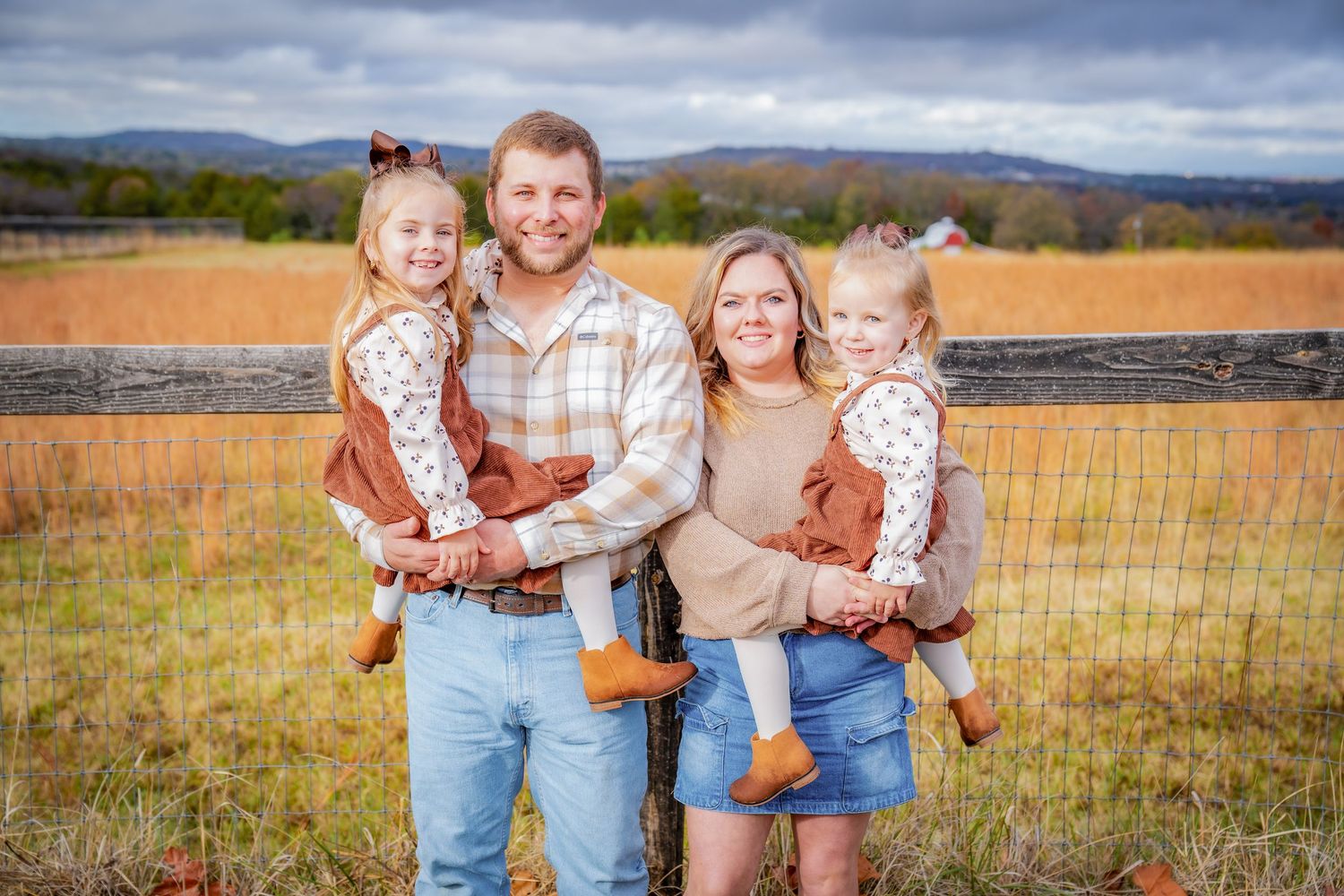 Family photo session in an autumn field with mountains and dramatic clouds in background.