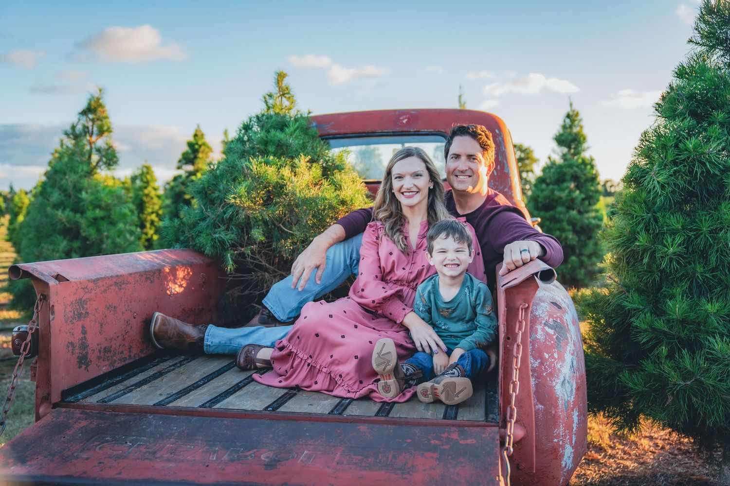 Family poses together near rustic red truck during golden hour photo session.