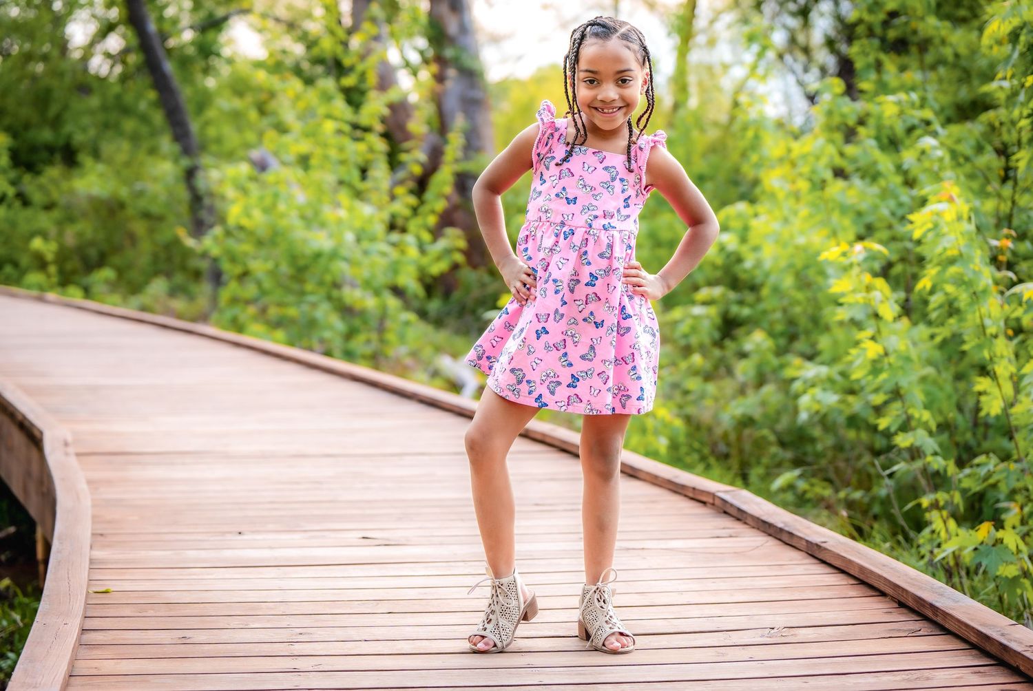 A pink floral dress and sneakers on a curved wooden boardwalk surrounded by lush green foliage.